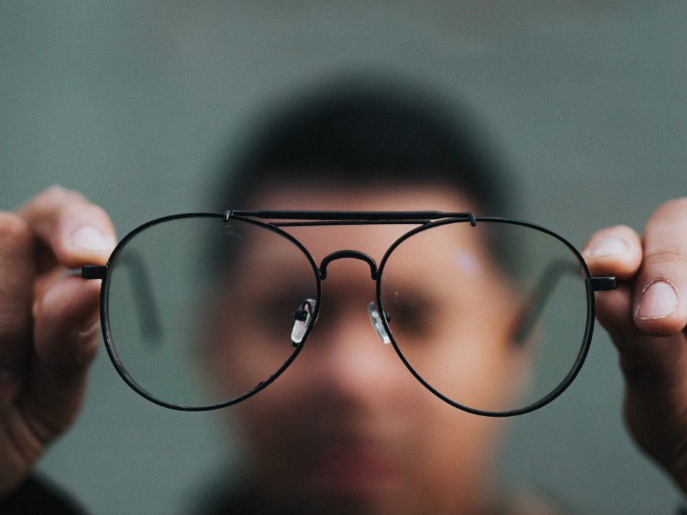 A man holding up a pair of glasses.