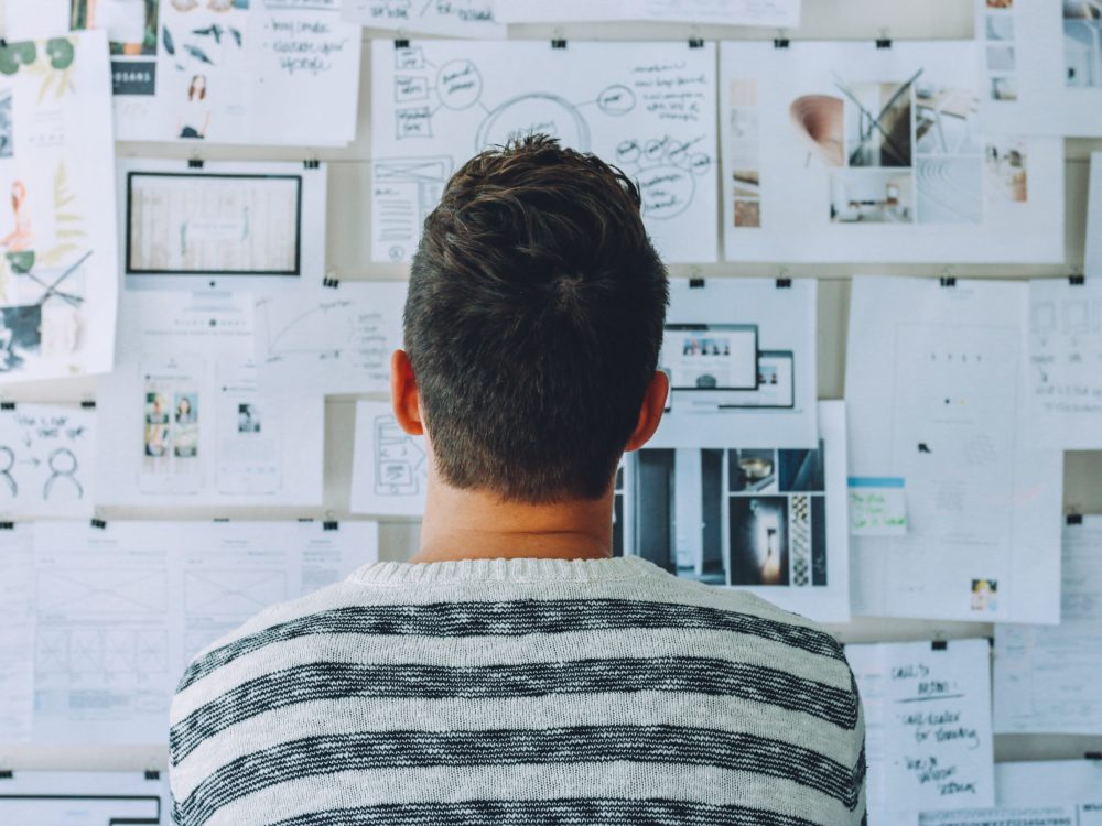 A man looking at a wall full of paper.